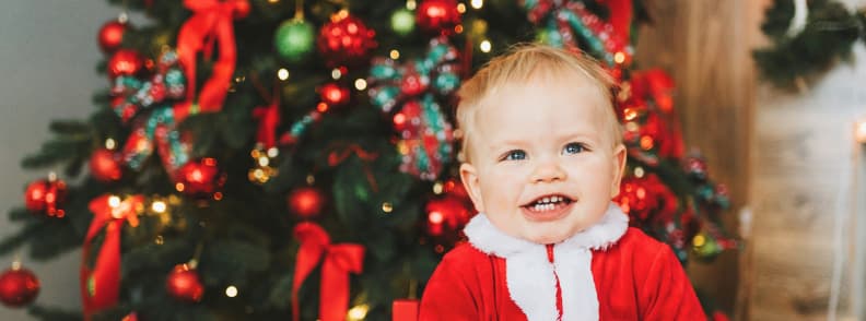 Enfant souriant en tenue rouge de Noel devant un sapin decore