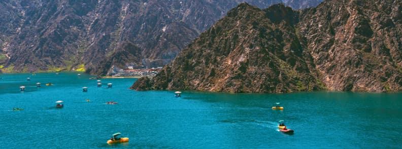 hatta dam lac activites nautiques dubai montagne Vue panoramique du Hatta Dam avec pédalos et kayaks sur le lac turquoise entouré de montagnes, attraction incontournable lors d’une excursion Hatta Dubaï