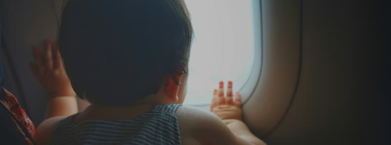 Un tout-petit regarde par le hublot pendant le vol, un moment de calme et de curiosité lors d’un voyage en avion en famille avec un jeune enfant.