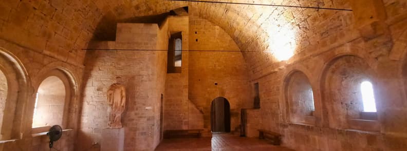 Ancien dortoir voûté de l’abbaye du Thoronet en Provence, espace monastique en pierre avec statues, fenêtres romanes et lumière tamisée
