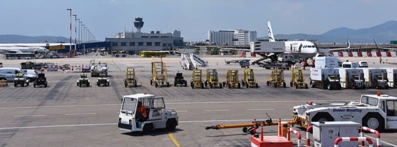 Comment aller de laeroport dAthenes au centre ville et retour metro bus taxi transfert prive comment aller à Athènes depuis l’aéroport. Vue sur le tarmac de l’aéroport international d’Athènes Elefthérios Venizélos avec avions au sol, véhicules de piste et terminal en arrière-plan avant un transfert aéroport Athènes centre-ville.