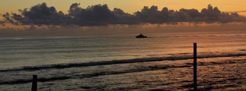 Bateau au large du port de Saint-Gilles au coucher du soleil sur la côte ouest de La Réunion avec ciel orangé et mer calme.