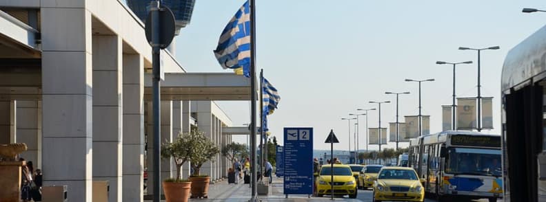 aeroport athenes bus taxi transport centre ville options Arrêt de bus et station taxi à l’extérieur de l’aéroport international d’Athènes avec bus express, taxis jaunes et drapeaux grecs le long du terminal des arrivées.