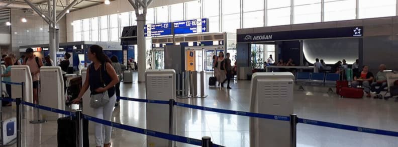 aeroport athenes terminal depart transport centre ville correspondences Zone d’enregistrement au terminal départ de l’aéroport international d’Athènes avec comptoir Aegean Airlines, passagers et panneaux indiquant les portes d’embarquement et les connexions vers le centre-ville.