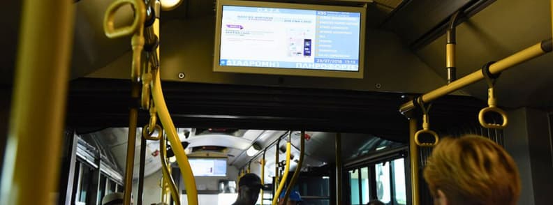 bus x95 aeroport athenes syntagma centre ville Intérieur du bus X95 aéroport Athènes avec écran d’information, passagers assis et barres de maintien jaunes pendant le trajet vers Syntagma centre-ville.
