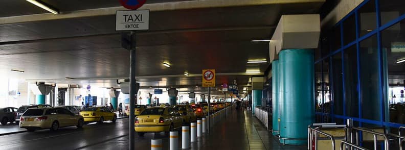 taxi aeroport athenes tarif centre ville officiel Station taxi officielle à l’aéroport international d’Athènes avec file de taxis jaunes sous le terminal des arrivées pour transfert vers le centre-ville.