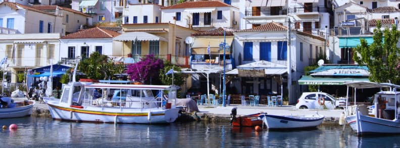 Bateaux amarrés dans le port de Poros en Grèce avec maisons blanches, volets colorés et terrasses en bord de mer lors d’une croisière d’une journée depuis Athènes