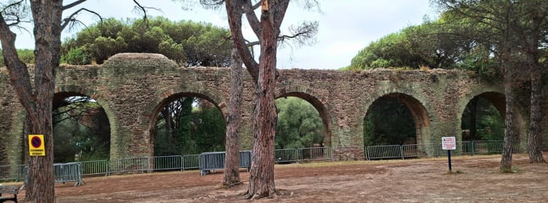 Arches en pierre de l’aqueduc romain de Fréjus dans le Parc Aurélien, avec des vestiges antiques entourés de pins méditerranéens et protégés par des barrières métalliques.