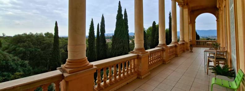 Terrasse à colonnade de la Villa Aurélienne à Fréjus, avec des balustrades en pierre, de grandes arcades et une vue sur les cyprès du Parc Aurélien et les collines au loin.