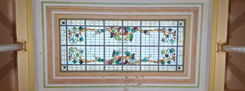 Verrière rectangulaire de la Villa Aurélienne à Fréjus, ornée de vitraux aux motifs floraux multicolores et entourée de moulures décoratives crème, dorées et vert pâle.