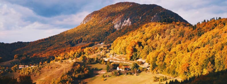 Cele mai bune vacante de toamna in Romania ghid de calatorie in Carpati Peisaj de toamnă în Munții Carpați din România, cu păduri colorate în nuanțe de galben, portocaliu și roșu, sate montane și lumini calde de apus