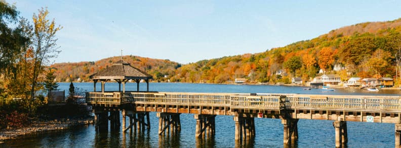 Ponton din lemn pe un lac liniștit înconjurat de păduri colorate, o scenă tipică pentru vacanțe de toamnă în Canada și escapade relaxante în natură.
