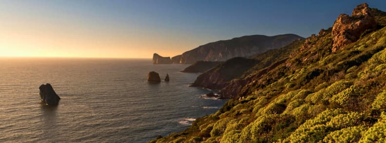 Sardinia toamna destinatie calda in octombrie Italia calatorii de toamna Peisaj de coastă în Sardinia la apus, cu stânci dramatice și mare liniștită scăldată în lumină aurie, una dintre cele mai populare destinații calde în octombrie din Marea Mediterană