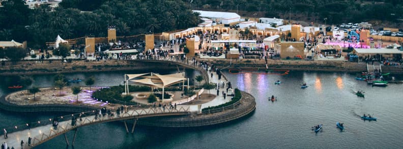 Hatta Wadi Hub activitati festivaluri aventura Emiratele Arabe Unite Vedere aeriană asupra Hatta Wadi Hub, cu turiști, festivaluri și activități în aer liber pe malul apei.