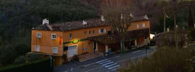 Hôtel Au Relais Provençal din Bagnols-en-Forêt, cu fațadă ocru, acoperiș din țiglă tradițională, intrare acoperită și trecere de pietoni în fața clădirii.