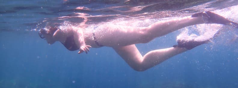 Femeie practicând snorkeling în apele albastre ale Mării Mediterane, în largul coastei din Saint-Raphaël, cu raze de soare pătrunzând prin apă și bule în jurul corpului.