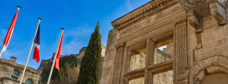 Fereastra renascentistă cu inscripția Post Tenebras Lux din Les Baux de Provence, alături de drapelul Franței și ziduri istorice