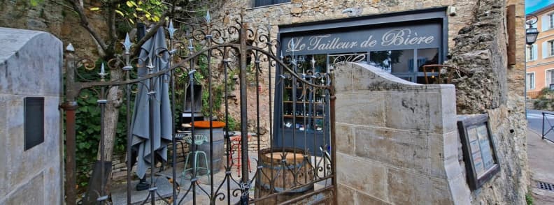Intrarea în Le Tailleur de Bière Cotignac, bar artizanal amenajat într-o clădire din piatră din Cotignac Provence Verte, cu poartă de fier forjat și terasă rustică