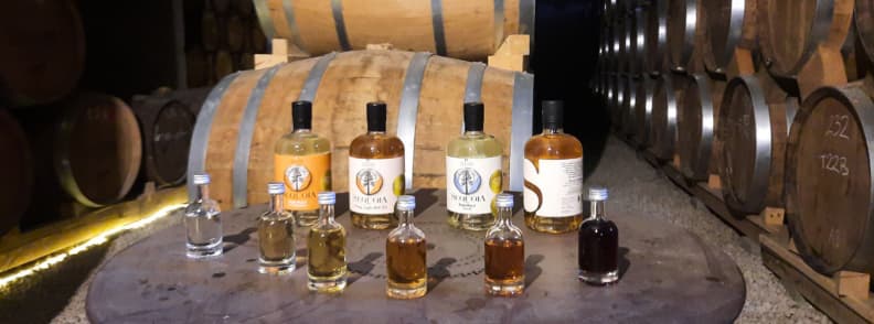 Sticle de whisky Sequoia asezate pe un butoi in pivnita de maturare a Distileriei din Vercors inconjurata de randuri de butoaie