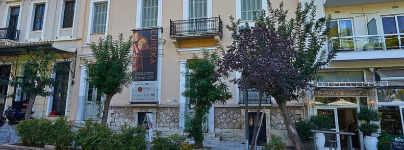 Muzee din Atena muzeul Herakleidon arta stiinta Fațada muzeului Herakleidon din Atena, amplasat într-o clădire neoclasică, cu bannere expoziționale și vegetație urbană.