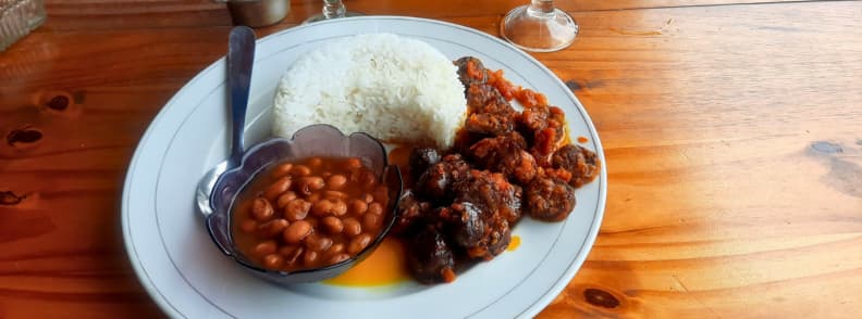 Farfurie cu rougail saucisse în estul insulei Reunion, servită cu orez alb și fasole roșie pe masă din lemn.