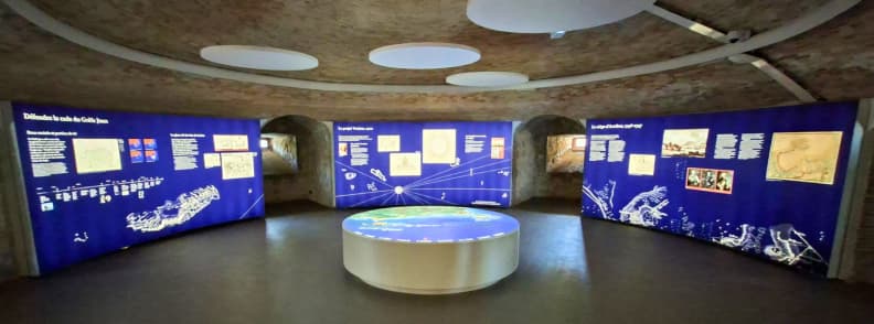 batterie du graillon antibes expozitie istorie militara posidonia Sală de expoziție din Batterie du Graillon Antibes, cu panouri albastre despre istoria militară a coastei, hărți, documente și o masă interactivă în cadrul Posidonia Antibes.