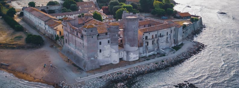 Vedere aeriană asupra Castelului Santa Severa, cu turnuri medievale, plajă și țărm stâncos lângă portul Civitavecchia