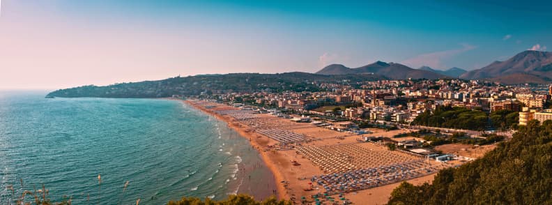 Ghid plaje langa Roma. Plajă întinsă cu nisip și șezlonguri pe coasta Lazio, lângă Roma, mărginită de oraș, dealuri și Marea Tireniană