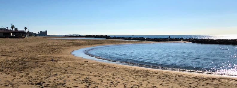 Golf cu nisip fin și apă calmă la Santa Marinella, protejat de diguri de piatră pe coasta din Lazio