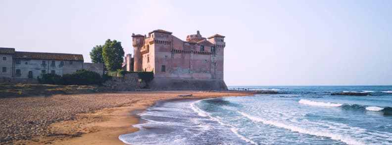 Castelul Santa Severa lângă plaja cu nisip, cu valurile Mării Tireniene și clădiri istorice pe coasta Lazio