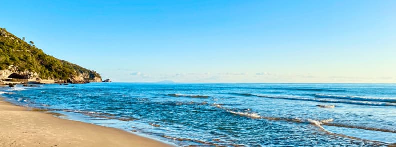 Plajă cu nisip fin și apă limpede în Sperlonga, mărginită de o coastă verde și stâncoasă în Lazio
