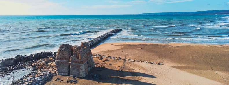 Ruine antice din cărămidă pe plaja Ladispoli, lângă un dig de piatră și valurile Mării Tireniene