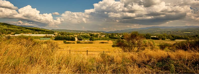 Provence Toamna Campuri Aurii Peisaj Rural Peisaj rural din Provence toamna, cu câmpuri aurii, vegetație uscată, dealuri împădurite și munți sub nori de toamnă.