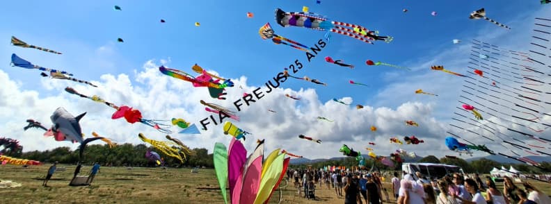Festival de l Air Frejus 2025 zmeie si aniversare 25 ani Zmeie colorate de diferite forme zboară deasupra publicului la Festival International de l’Air Fréjus 2025, sub instalația aniversară FIA Fréjus 25 ans.
