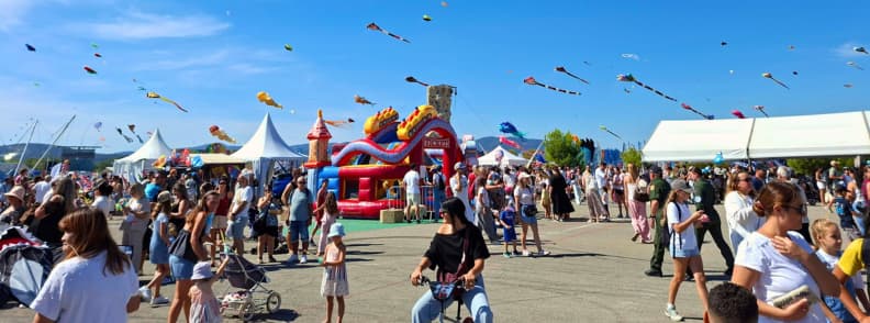 Festival de l Air Frejus activitati copii si ateliere de zmeie Familii cu copii printre corturi, ateliere și jocuri gonflabile la Festival International de l’Air Fréjus, cu zmeie colorate zburând deasupra Base Nature François Léotard.