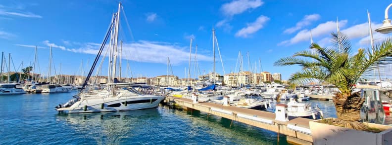 Port Frejus marina velier si acces Festival de l Air Veliere și ambarcațiuni acostate în marina Port-Fréjus, cu palmieri și clădiri pe mal, aproape de Base Nature François Léotard și Festival International de l’Air Fréjus.