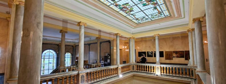 Atriumul central al Villa Aurélienne din Fréjus, cu luminator din vitralii florale, coloane decorative, balustrade sculptate și galerie interioară cu fotografii expuse.