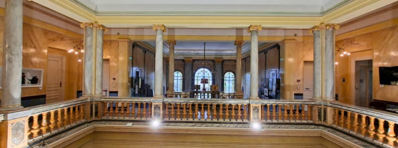 Galeria peristilului din Villa Aurélienne din Fréjus, cu coloane cu aspect de marmură, capiteluri aurii, balustrade sculptate și ferestre arcuite cu vitralii.