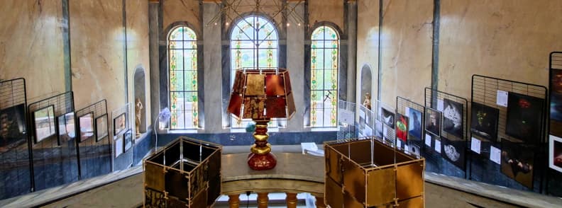 Scara istorică din Villa Aurélienne din Fréjus, cu trei ferestre arcuite cu vitralii florale, fotografii expuse pe pereți și obiecte decorative în prim-plan.