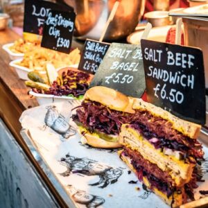 East End Food Tour. Salt beef sandwich served at a London market stall with price signs and sides