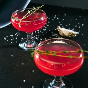 Soho food and cocktail tour. Two red cocktails served in coupe glasses on a dark table with garnish