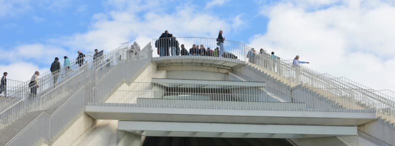 Pyramid of Tirana Climb Rooftop Stairs and City Views Visitors climbing the white exterior staircases of the Pyramid of Tirana, with viewing terraces rising above the former communist-era monument.