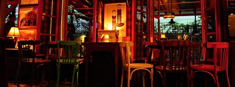 Radio Bar Tirana Best Time to Visit Blloku Colorful seating inside Radio Bar Tirana with mismatched chairs, warm lamps, framed artwork, mirrors, and views toward the covered courtyard.