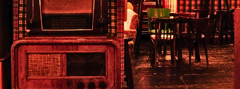 Radio Bar Tirana Practical Guide Blloku Interior Vintage radios and mismatched chairs inside Radio Bar Tirana, with warm red lighting, patterned fabric, and compact seating in Blloku.