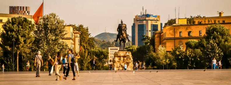 Skanderbeg Square Tirana Historic Center and Monument Skanderbeg Square in Tirana with the equestrian Skanderbeg statue, Albanian flag, surrounding historic buildings, trees, and Mount Dajti in the distance.