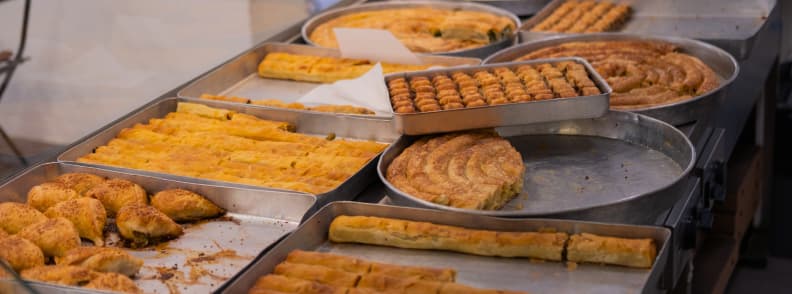 Tirana Food Guide Albanian Pastries Byrek and Baklava Trays of Albanian pastries in a Tirana bakery, including spiral and layered savory pies alongside rows of sweet pastries and baklava.