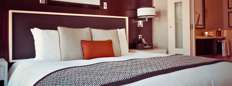 Where to Stay in Tirana Hotels and Accommodation Modern hotel room in Tirana with a large double bed, patterned bed runner, burgundy headboard, bedside lighting, and warm contemporary decor.