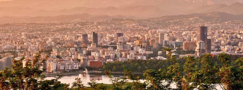 Why Visit Tirana Albania Panoramic City View Panoramic view of Tirana, Albania, with the city skyline, Grand Park lake, dense neighborhoods, and mountains surrounding the capital.