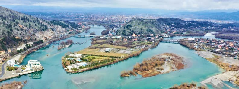 Shkoder Travel FAQ Albania Rivers City Panorama Aerial panorama of Shkodër, Albania, where the Buna, Drin, and Kir river system spreads around green islands, bridges, farmland, and the city below.