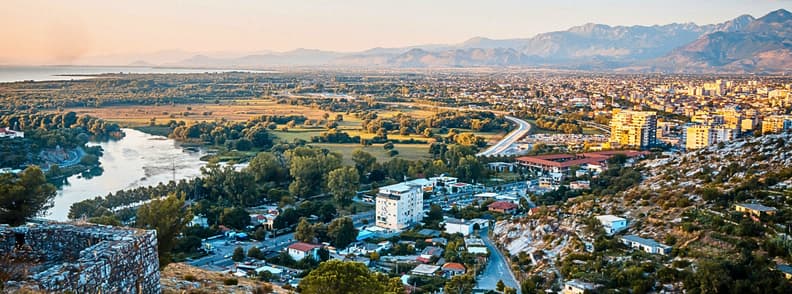 Best things to Do in Shkoder Albania. Panoramic view over Shkoder, Albania, from Rozafa Castle, with the Buna and Drin rivers, city skyline, fields, and mountains at sunset.